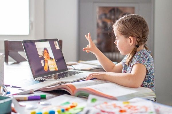 Young girl participating in an online learning session via laptop, books and stationery on the table.